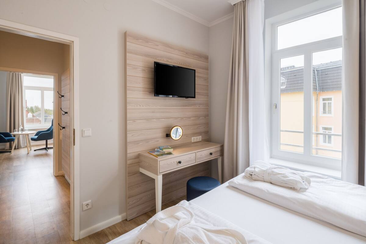 A hotel room with a bed, a desk with a TV, a mirror, and a window with curtains.