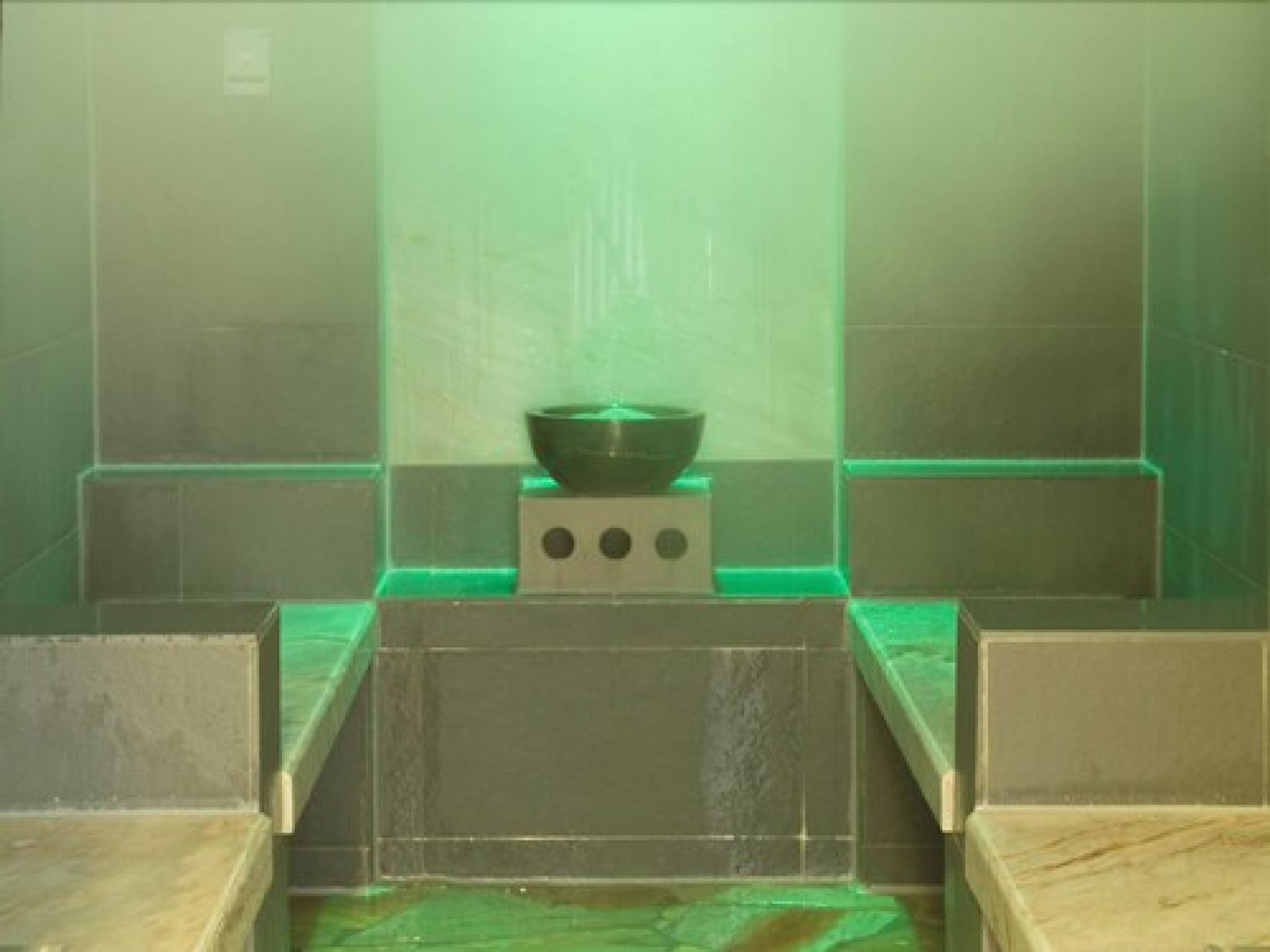Un baño con un lavamanos iluminado en verde, un espejo y suelo de baldosas.