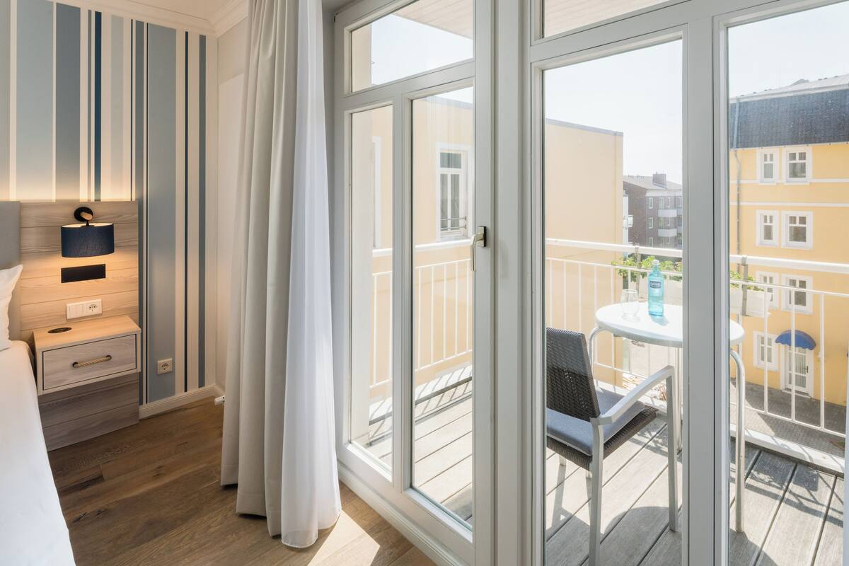 A hotel room with a balcony, a bed, a bedside table, and a window with curtains.