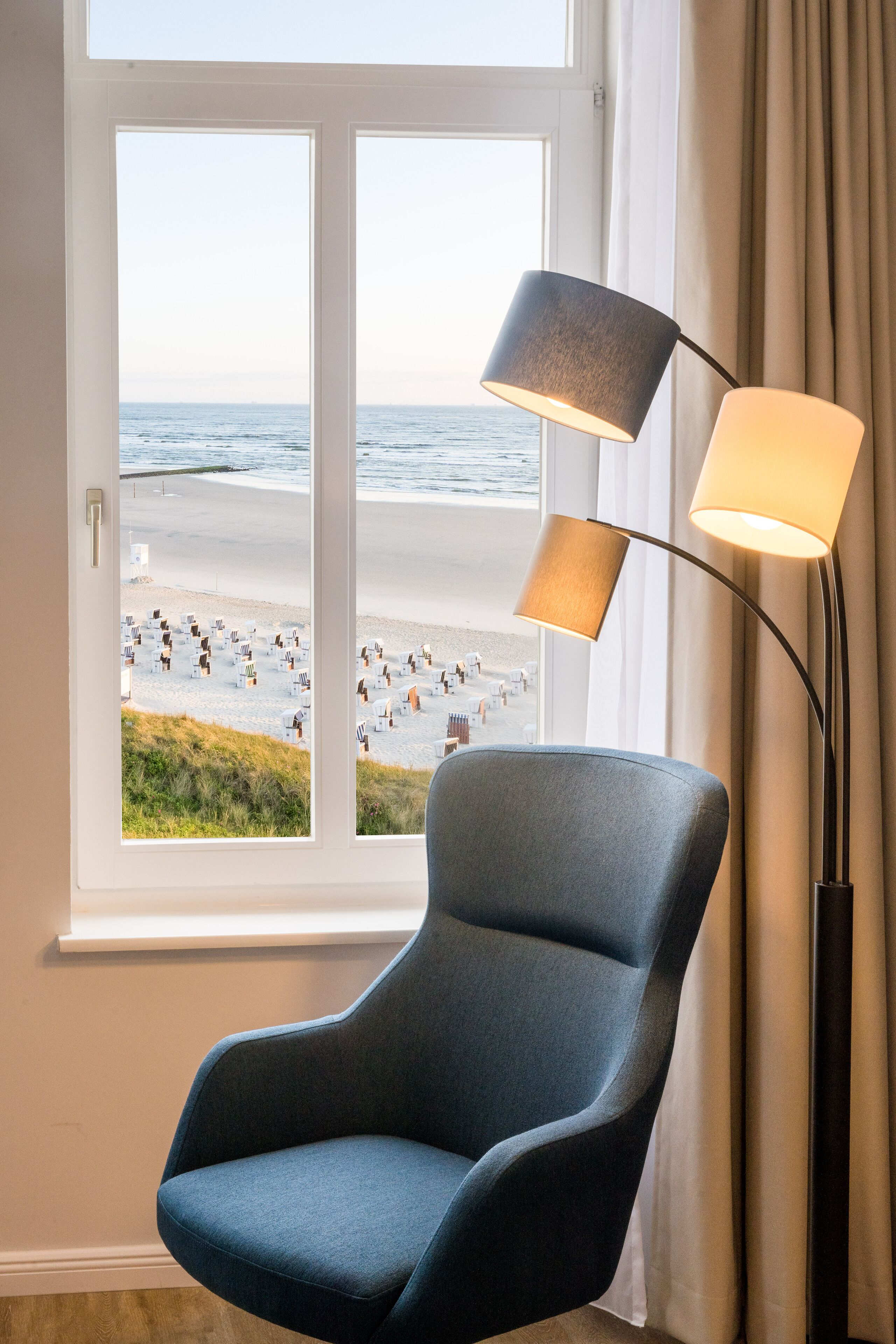 A room with a view of a beach, a blue armchair, and a floor lamp.