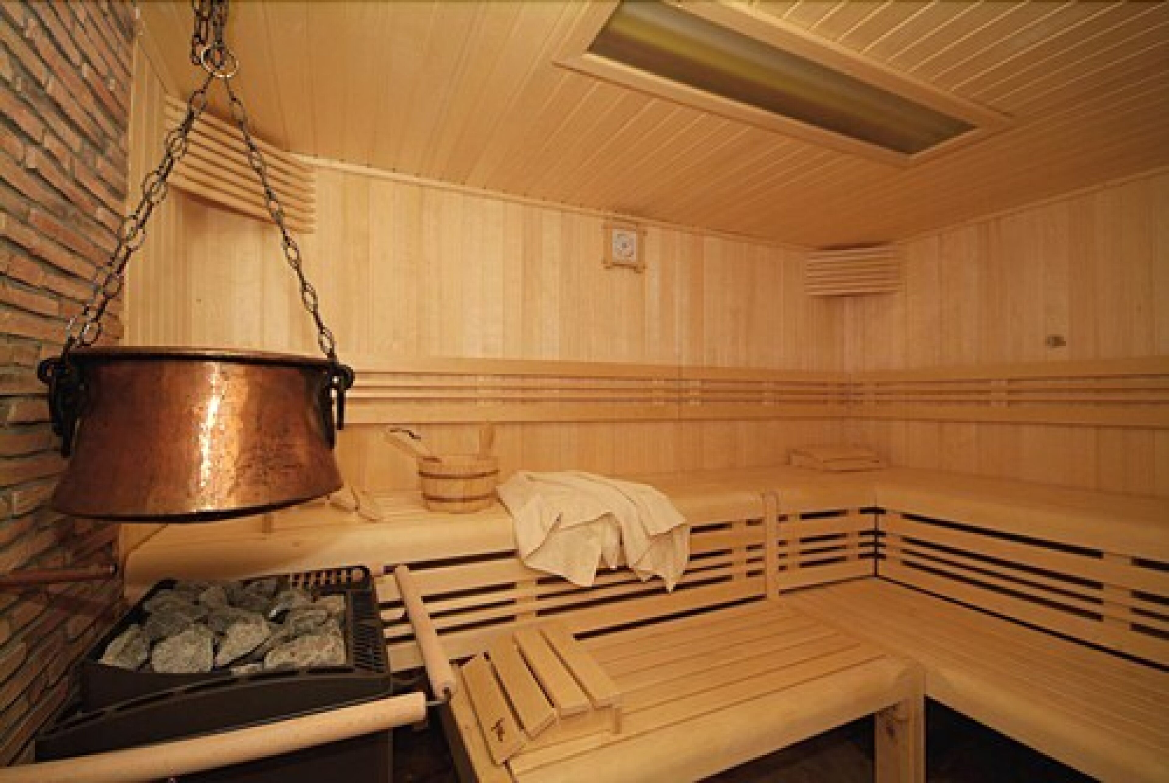 Una sauna con bancos de madera, una olla de cobre colgante y un calentador de piedra.