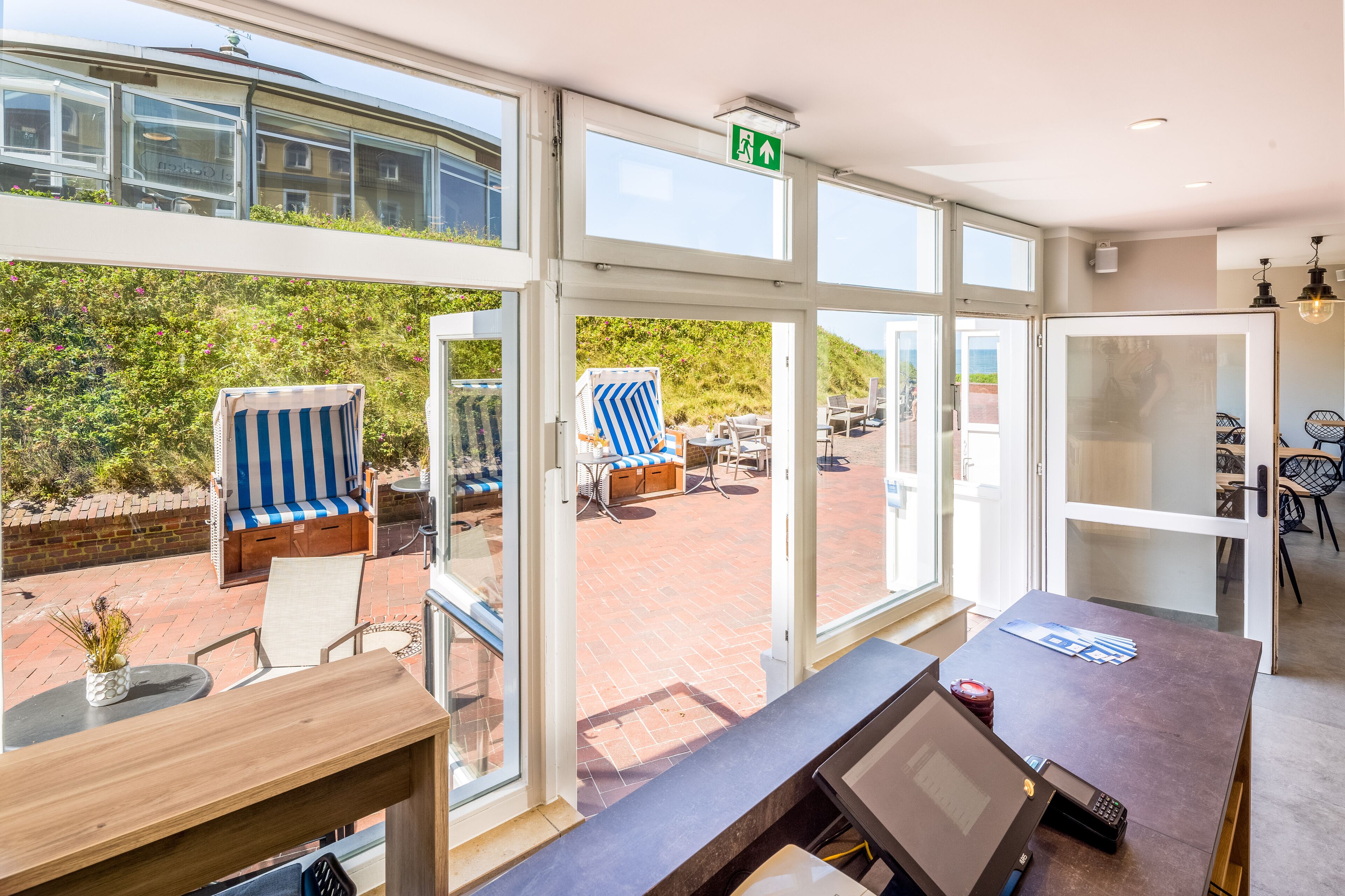 A hotel room with a large window, a wooden desk, a striped chair, and a view of the outdoor patio.