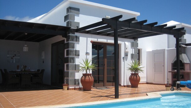 Un espace piscine agrémenté d’une pergola, de plantes en pot et d’une terrasse carrelée.