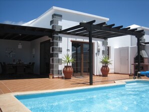 Un espace piscine agrémenté d’une pergola, de plantes en pot et d’une terrasse carrelée.