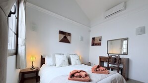 Un lit bien fait, avec une couette blanche et deux serviettes roses, une lampe de chevet et une table de chevet en bois.