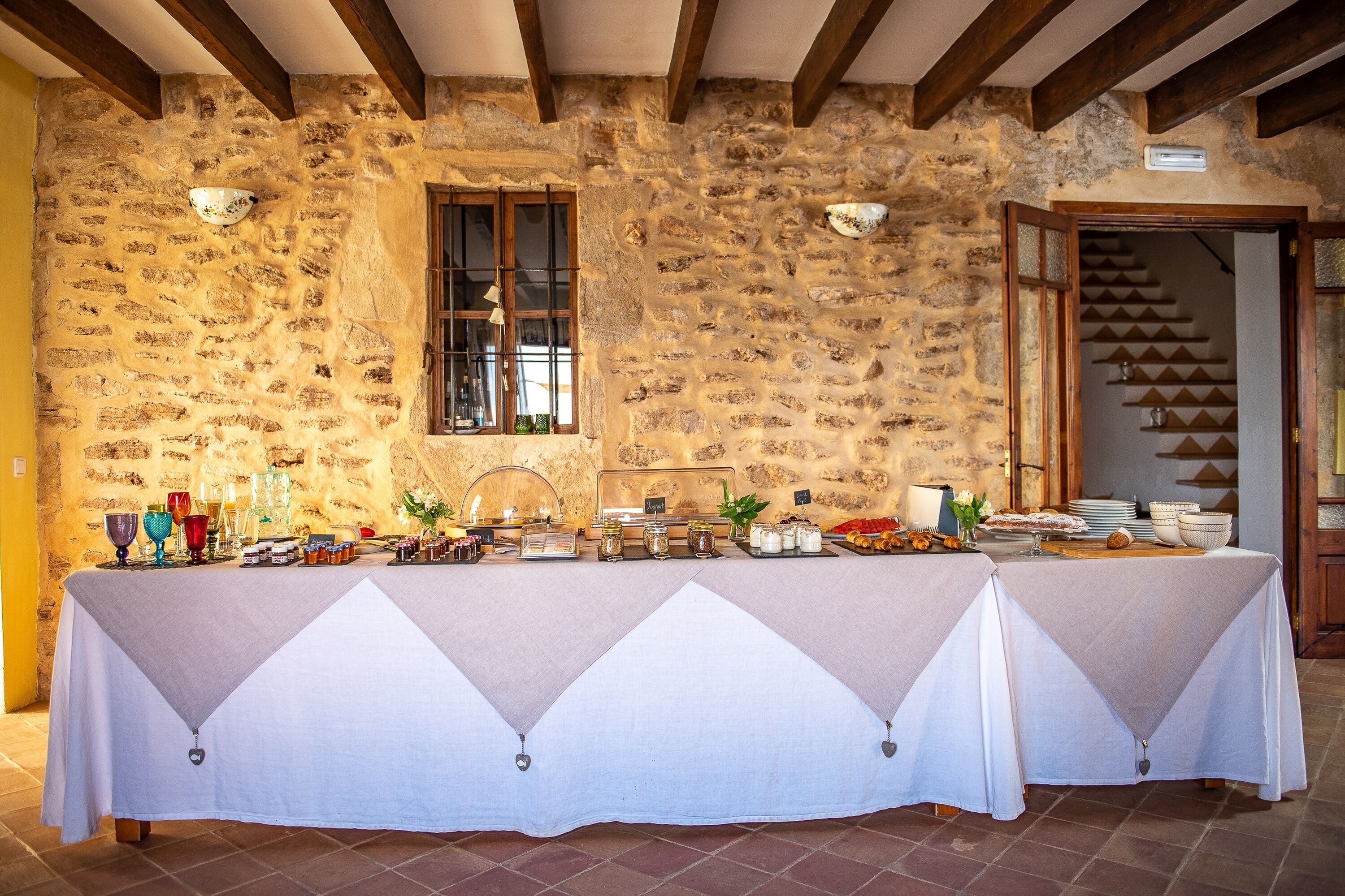 A stone-walled room with a buffet table covered in a white cloth, featuring various food items and glassware.