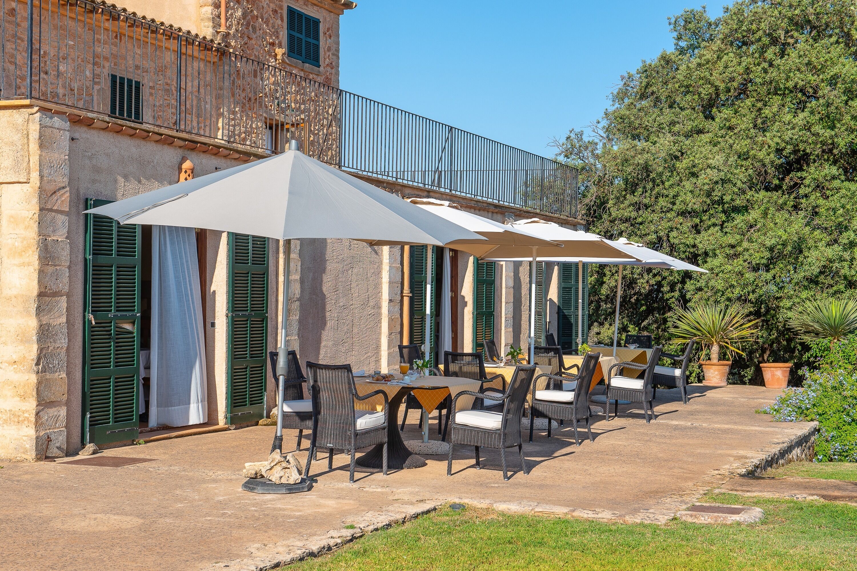 An outdoor patio with tables and chairs, surrounded by stone walls and green shutters.