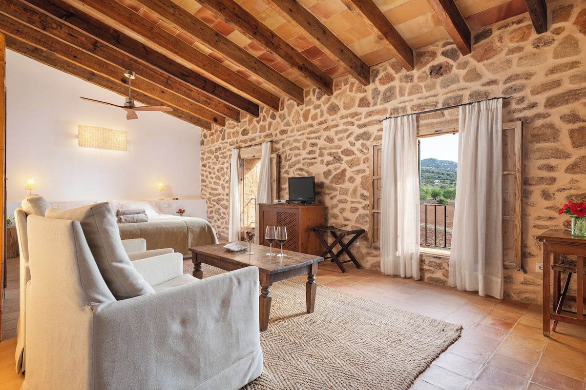 Una habitación acogedora con pared de piedra, techo de madera, cama, sofá, televisor y vistas al exterior.