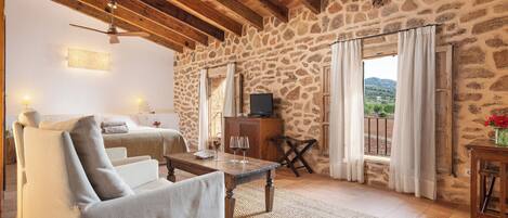 Um quarto aconchegante com parede de pedra, teto de madeira, cama, sofá, televisão e vista para o exterior.