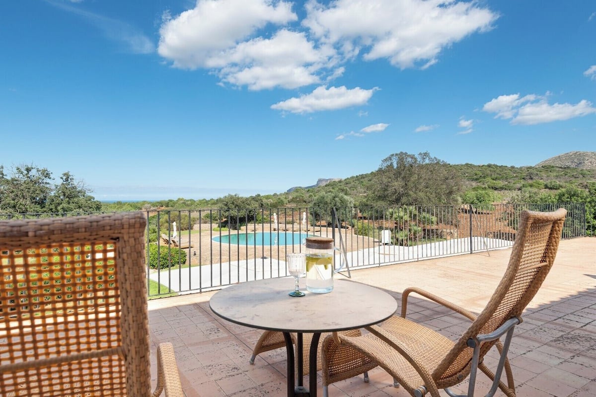 Una terraza con mobiliario de mimbre, una mesa redonda y vistas a una piscina y follaje.
