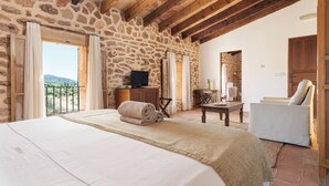 A bedroom with a stone wall, wooden beams, a bed with a rolled towel, a TV, and a view of the outdoors. - Finca Sos Ferres D'en Morey (Manacor)