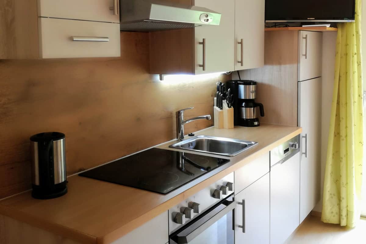 A modern kitchen with a built-in oven, a coffee maker, and a flat-screen TV mounted above the counter.