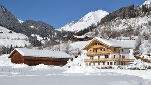 Un paysage montagneux enneigé, avec des bâtiments en bois, notamment un chalet doté de balcons et une grange.