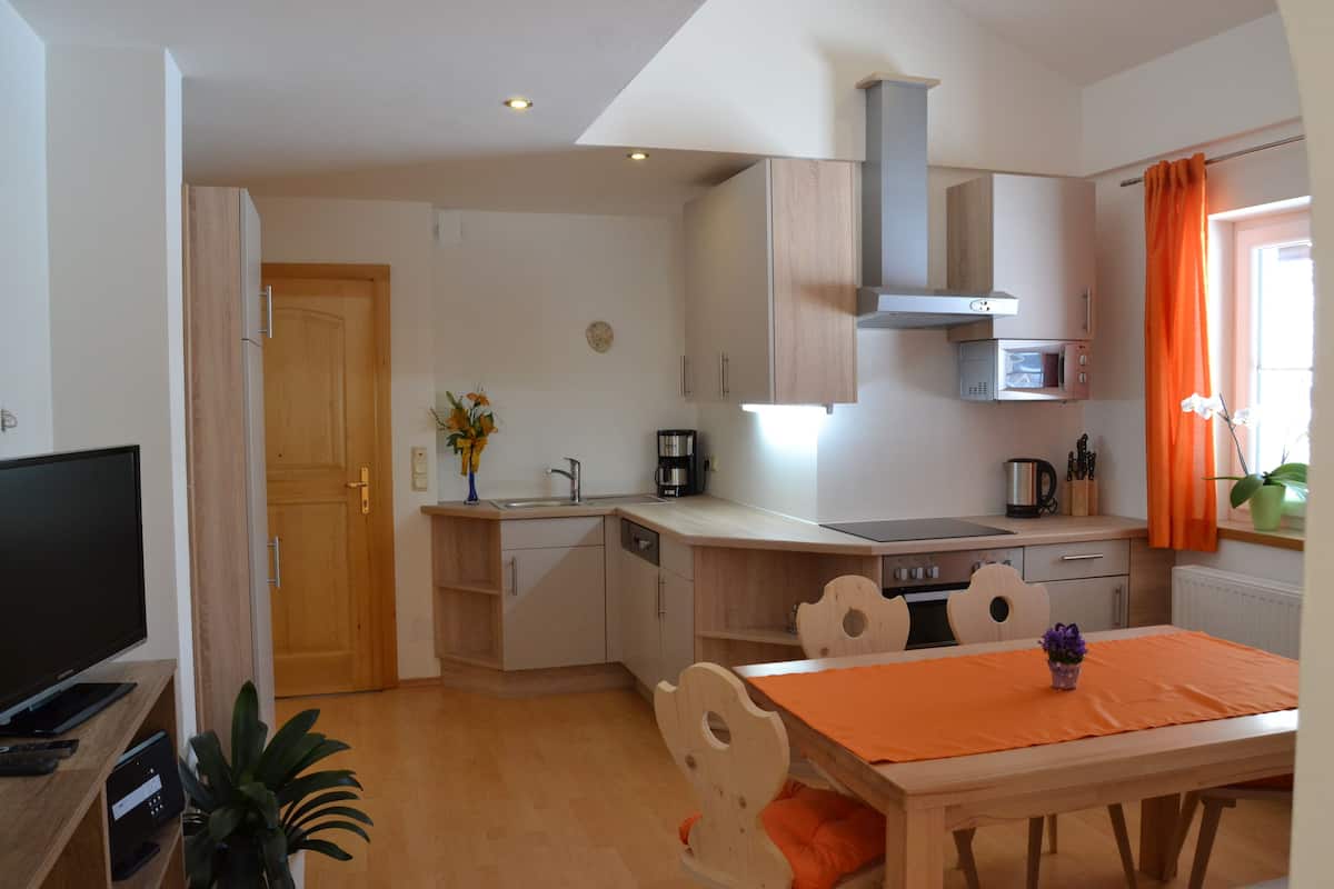 A compact kitchen with a microwave, stove, and sink. There is a dining table with chairs and a TV in the corner.