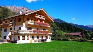 Un chalet à plusieurs étages doté de balcons, d’une pelouse bien entretenue et surplombant un paysage montagneux.