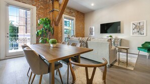 Un comedor con una mesa y sillas de madera, un sofá, un televisor y un balcón con vistas.