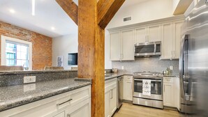 Una cocina moderna con armarios blancos, electrodomésticos de acero inoxidable y una pared de ladrillo decorativa.