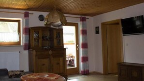 A living room with a wooden ceiling, a round coffee table, a sofa, a cabinet, and a television. - FeWo Konstandin (Bischofsmais)