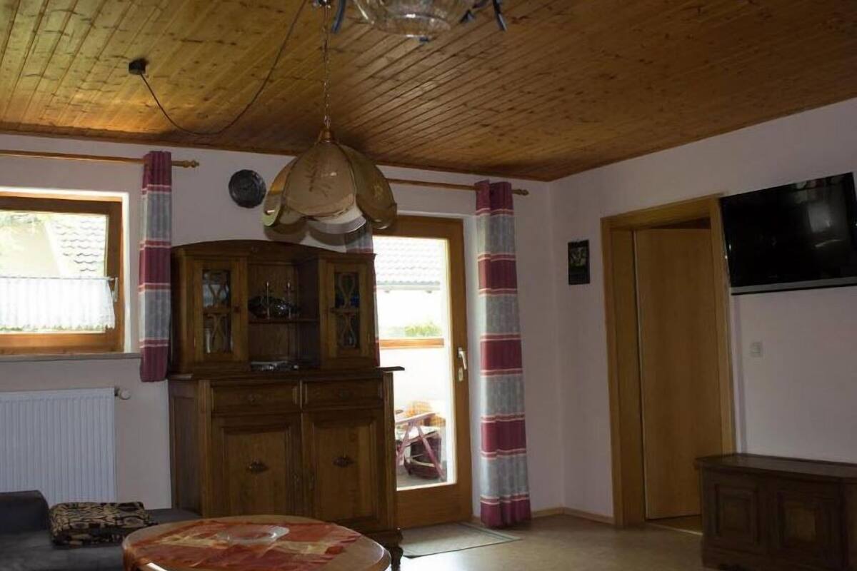 Una sala de estar con techo de madera, una mesa redonda para café, un sofá, un mueble aparador y un televisor.