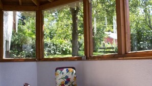 A room with a table and two chairs, large windows with a view of trees and a red building outside. - FeWo Konstandin (Bischofsmais)