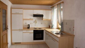 A compact kitchen with white cabinets, a black oven, a stainless steel sink, and a window with curtains. - FeWo Konstandin (Bischofsmais)
