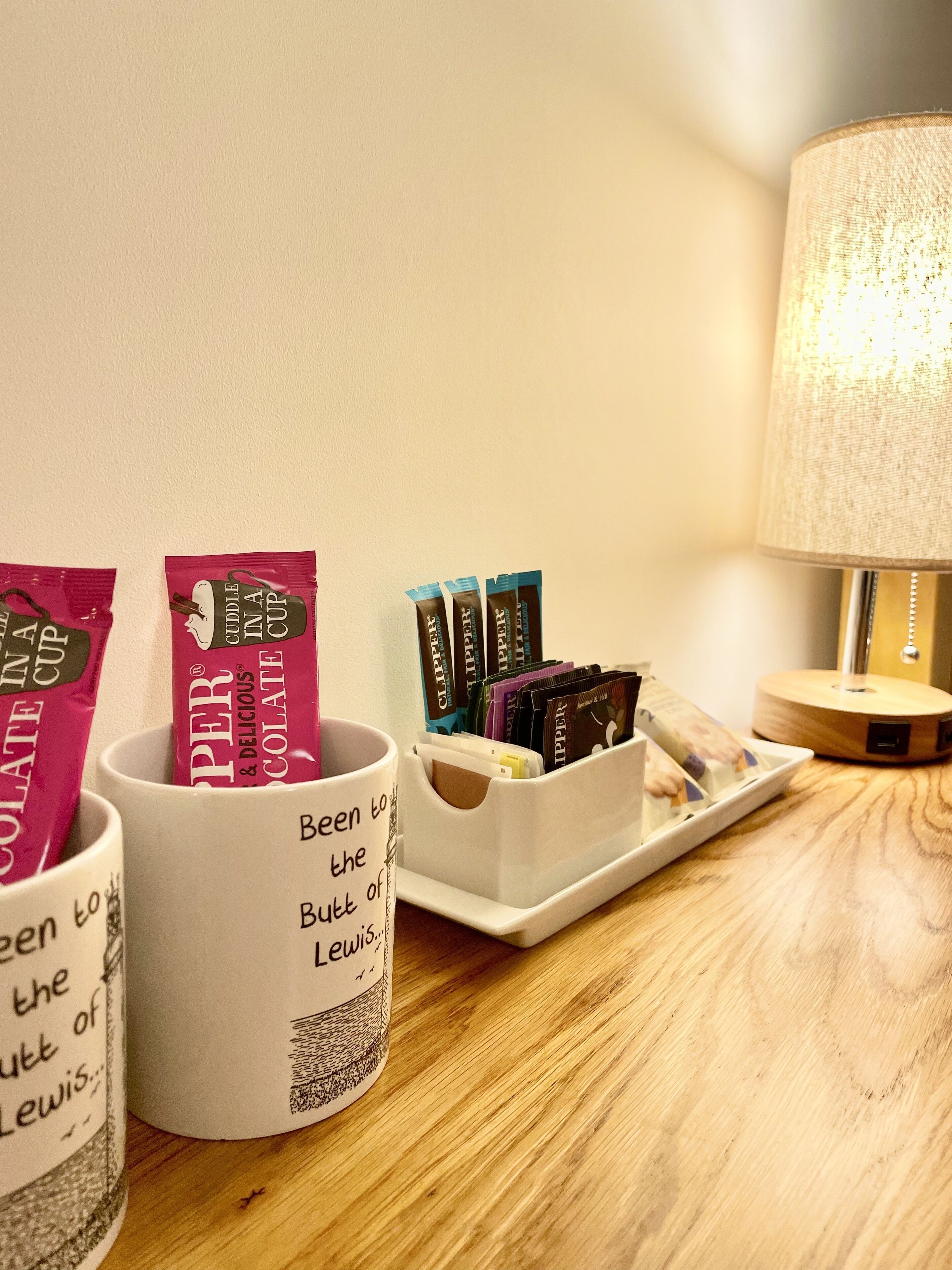 A table with two mugs, a tray with books, and a lamp.