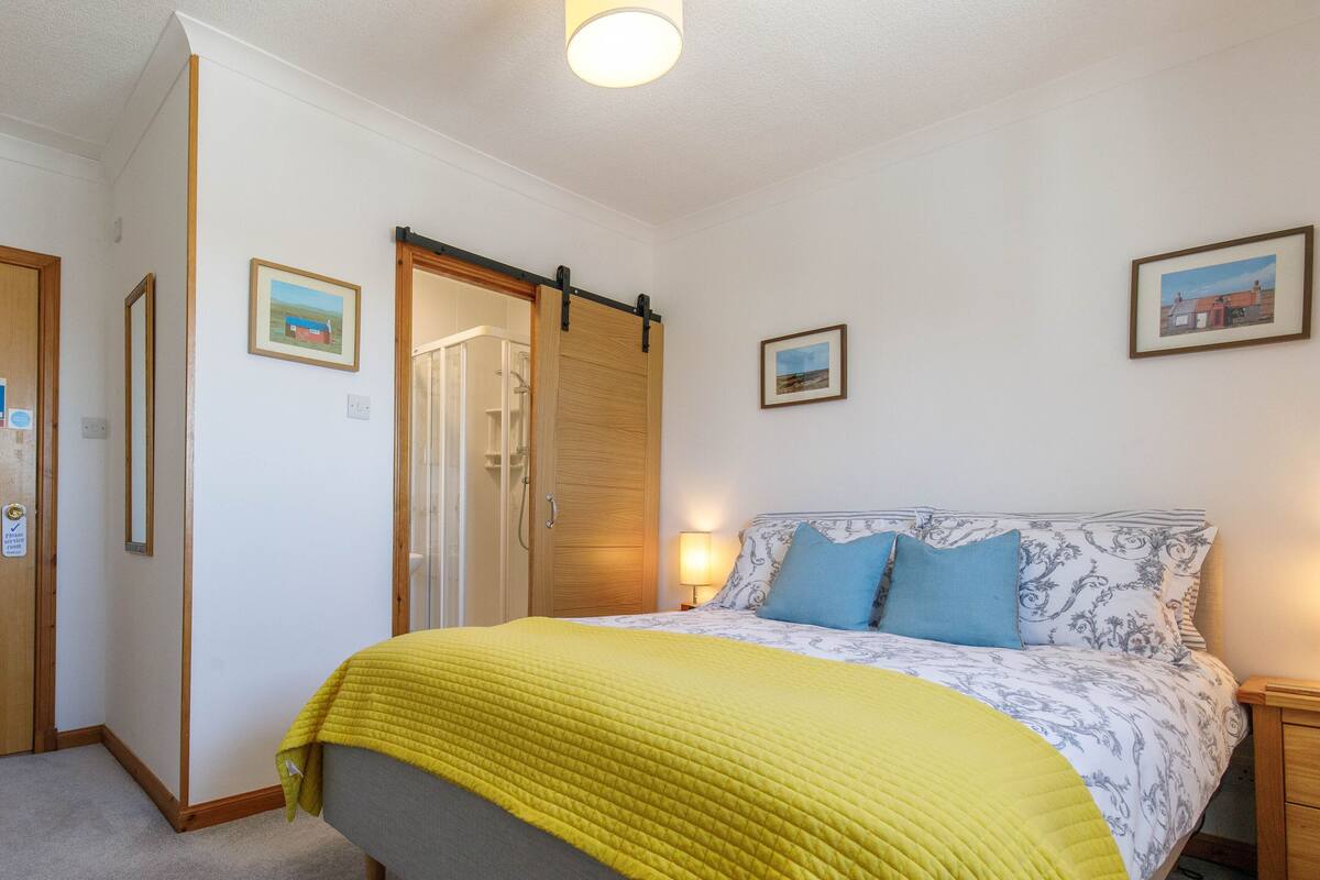 A bedroom with a bed, a sliding door, a nightstand, and framed pictures on the wall.