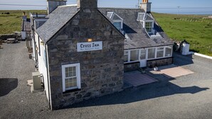 A stone building with a sign reading "Cross Inn Bar Restaurant Rooms." It features a sloped roof, multiple chimneys, and a gravel driveway. - Cross Inn (Isle of Lewis)
