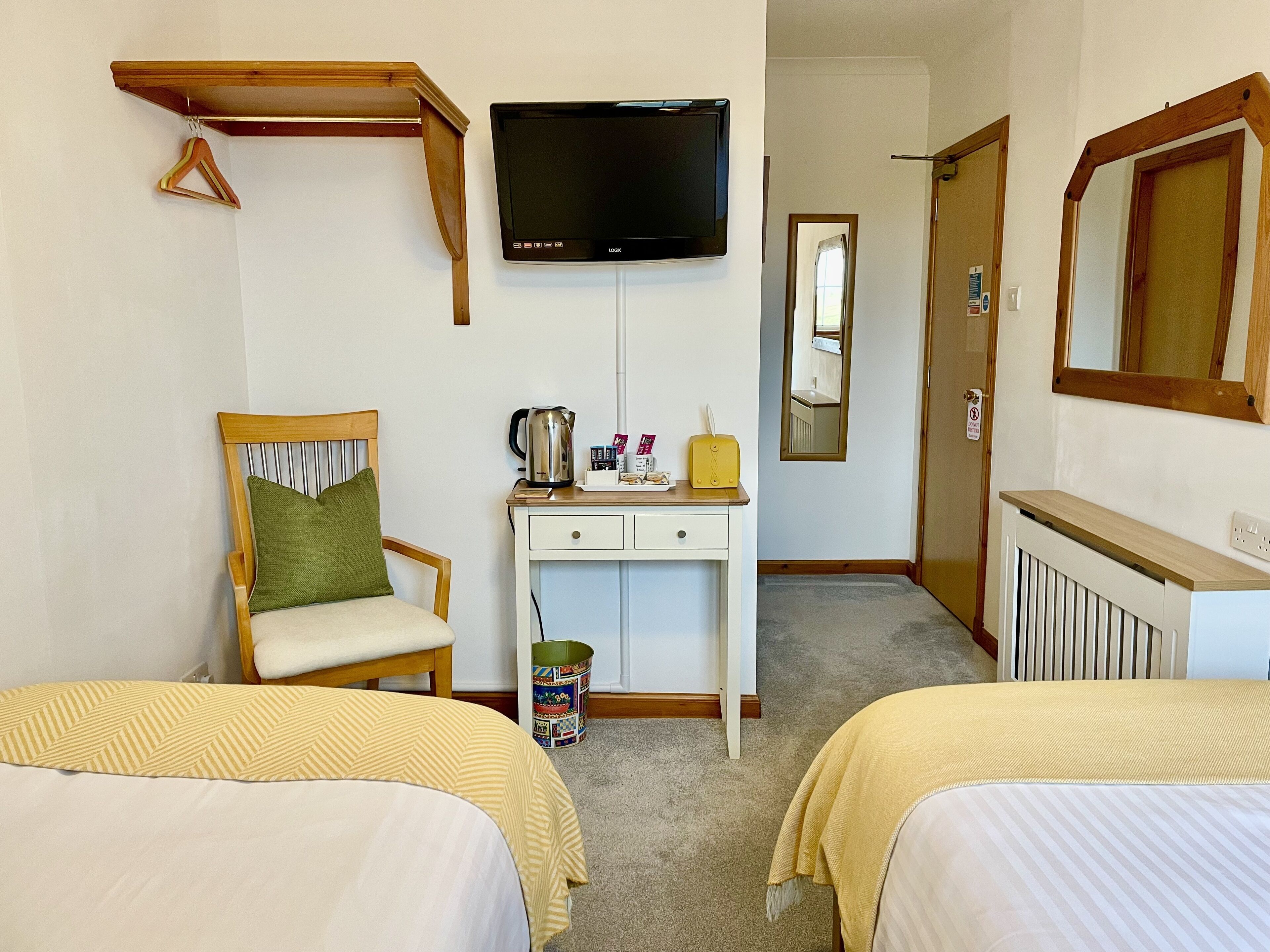 A hotel room with two beds, a desk with a kettle, a television, and a mirror.