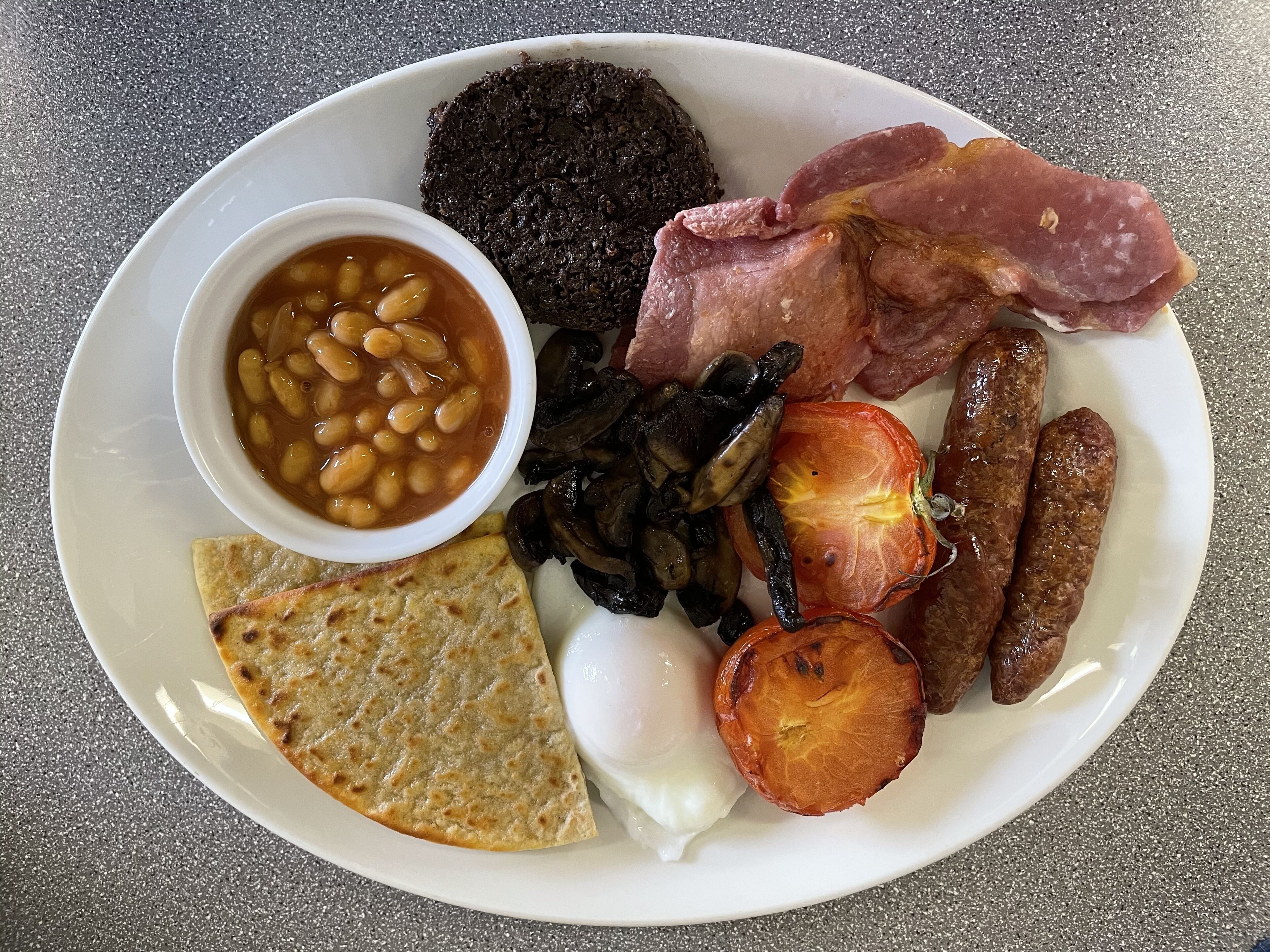 A plate of food including beans, mushrooms, sausages, ham, and a boiled egg.