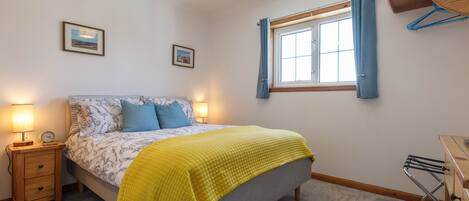 Un dormitorio con cama, lámparas de noche, una ventana con cortinas, una mesita de noche de madera y un tendedero fijado a la pared.