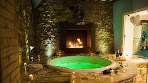 A stone-walled room with a green-lit jacuzzi, a fireplace, and candles.