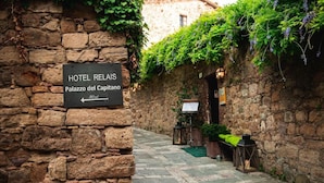 A stone wall with a sign for Hotel Relais, Palazzo del Capitano, and a narrow cobblestone path.