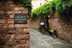 Un muro de piedra con un letrero que indica Hotel Relais, Palazzo del Capitano, y un estrecho camino adoquinado.