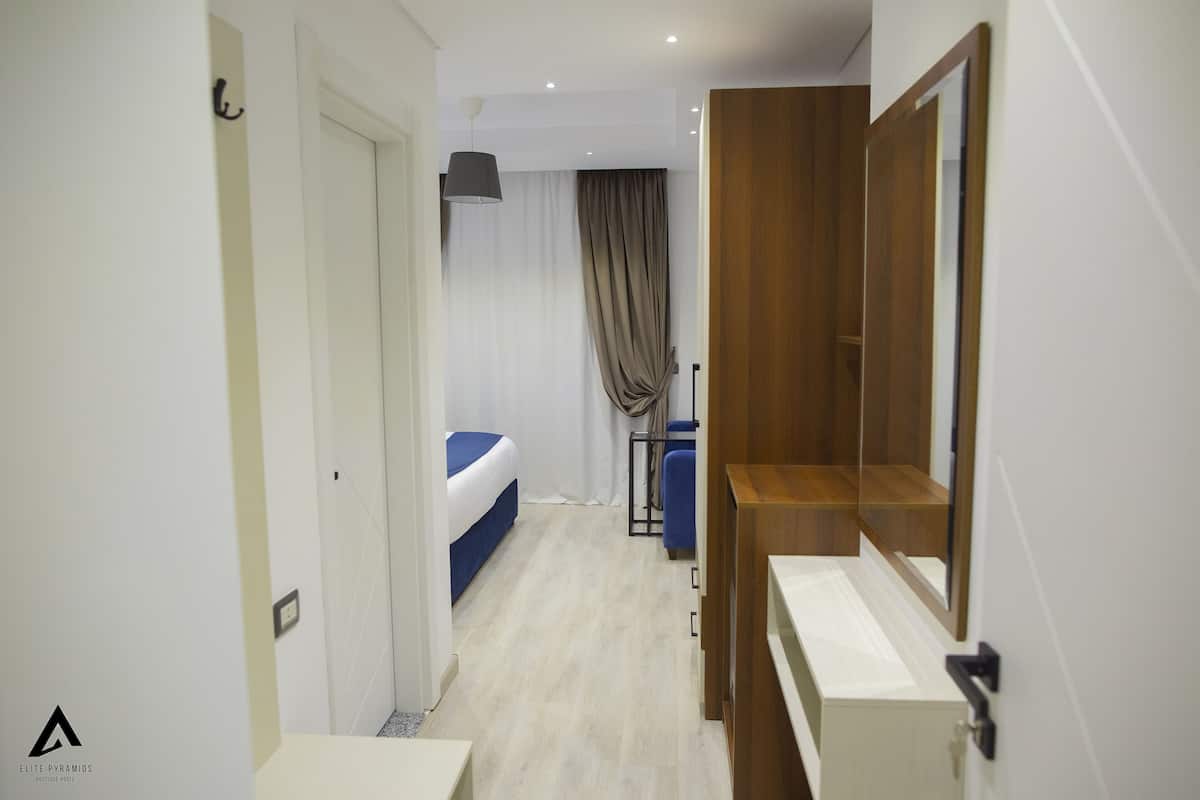 Moderni hotellihuone, jossa on sänky, peilillä varustettu meikkipöytä, puinen vaatekaappi ja vaaleanvärinen lattia.