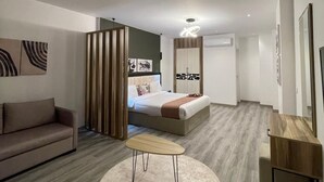 A modern hotel room with a sofa, a round table, a bed with a wooden headboard, and a large mirror. - Elite Pyramids Boutique Hotel (Giza)