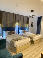 A hotel room with two beds, a modern chandelier, and a large abstract wall design.