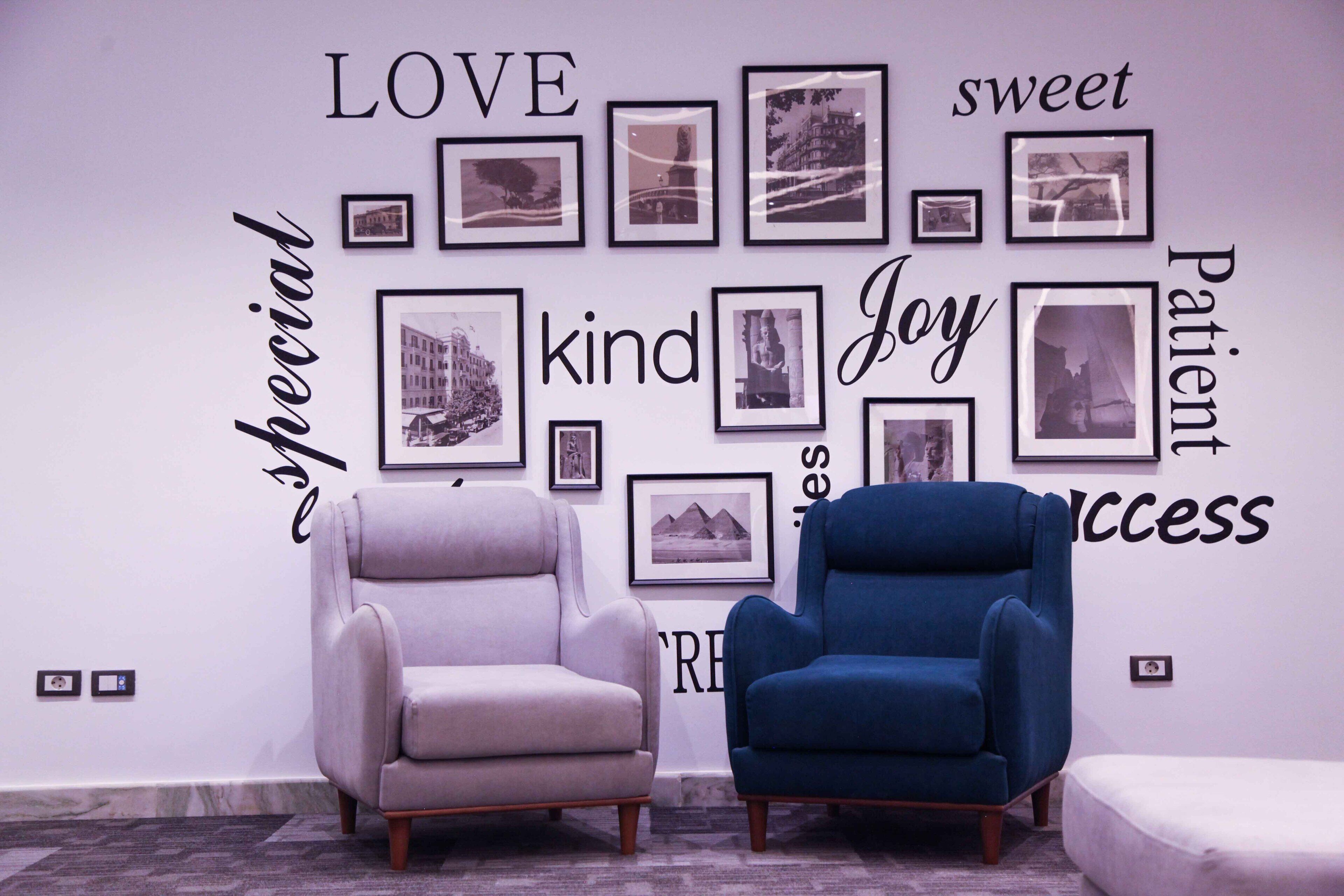 Quarto com duas poltronas e uma parede decorada com fotografias emolduradas e palavras inspiradoras.