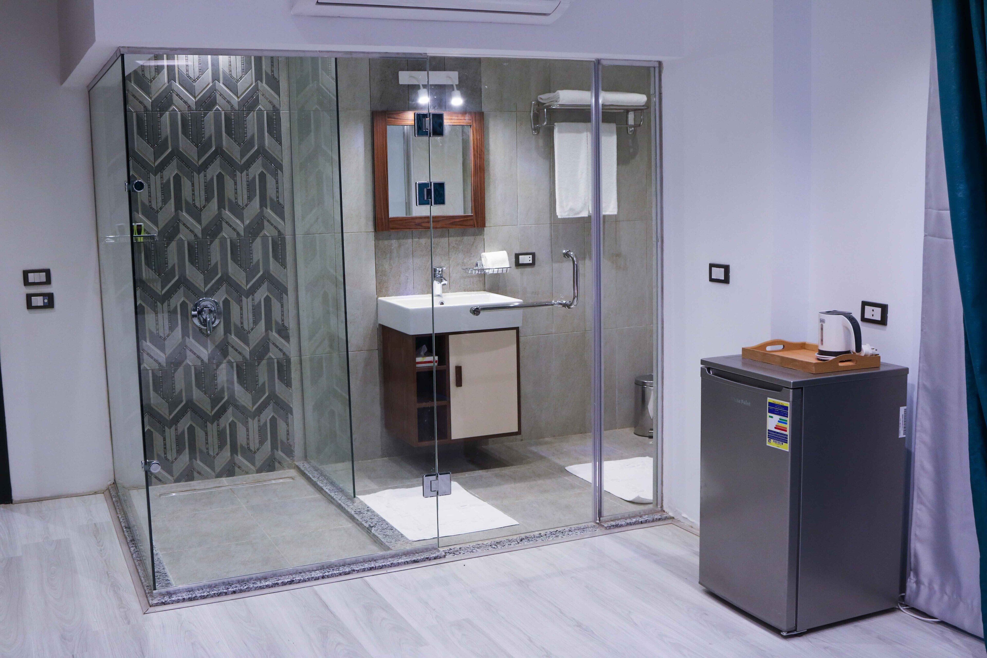 A modern bathroom with a glass-enclosed shower, a sink with a mirror, and a refrigerator.