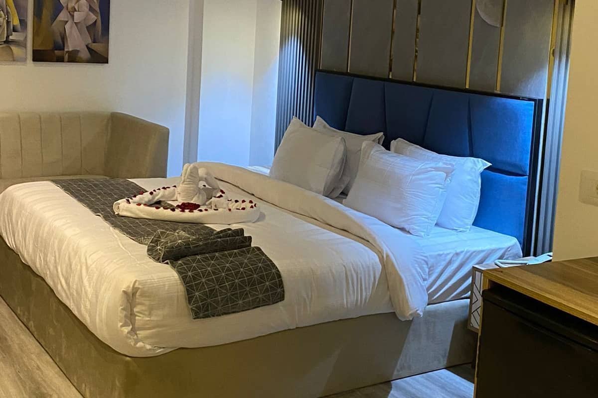 Una habitación de hotel moderna con una cama grande, una mesita de noche de madera y un aplique de pared.