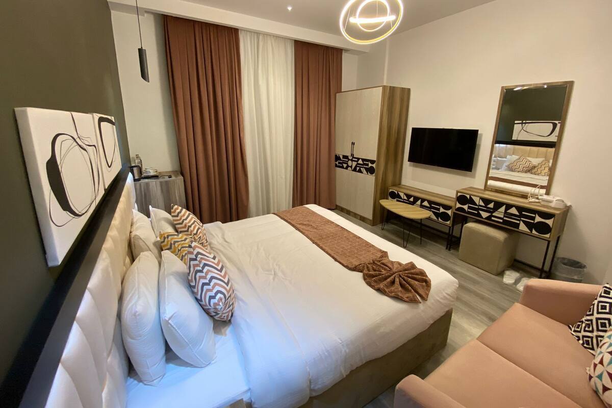 Moderni hotellihuone, jossa on suuri sänky, työpöytä tuolilla, televisio ja peili.