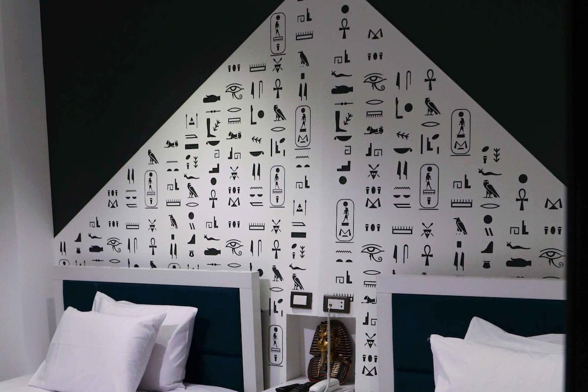Hotellihuone, jossa on kaksi sänkyä, tummanvihreä tehosteseinä ja seinä, joka on koristeltu hieroglyfeillä.