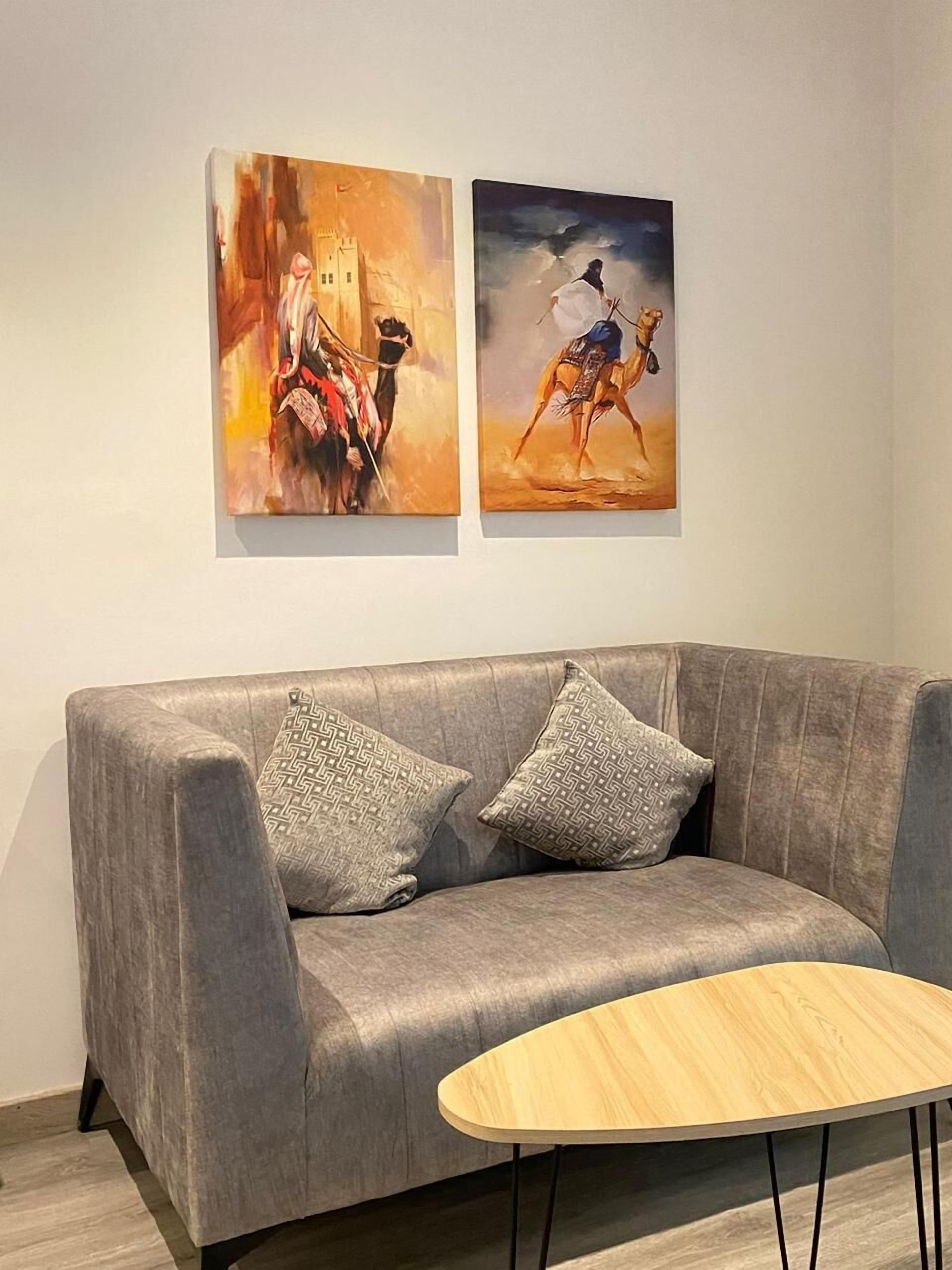 A grey sofa with two patterned cushions, a small wooden table, and two paintings on the wall.