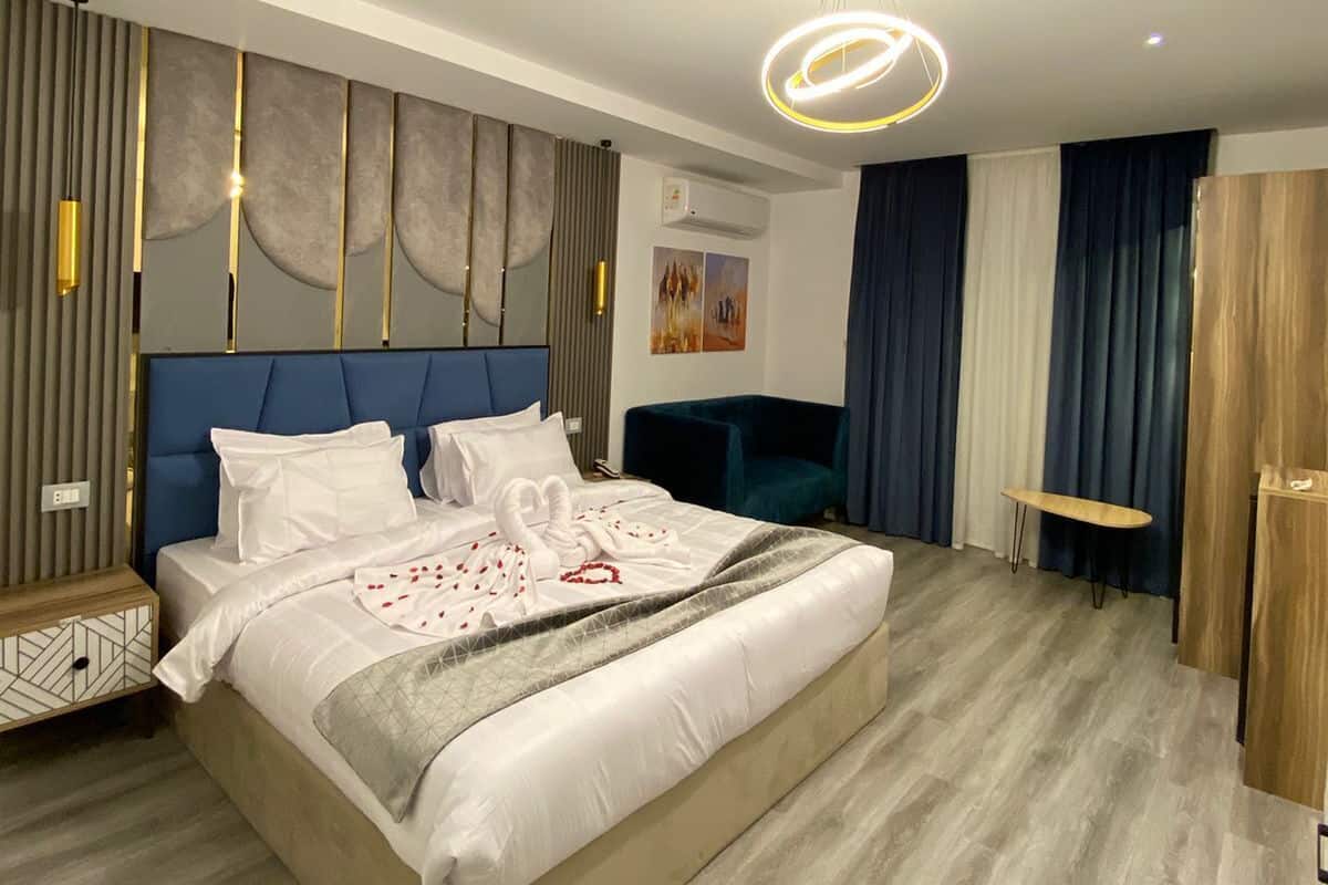 Moderni hotellihuone, jossa on suuri sänky, sininen pääty, puinen yöpöytä, pieni työpöytä ja puinen vaatekaappi.
