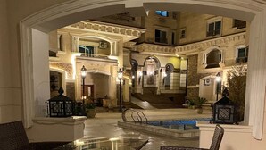 An outdoor seating area with wicker furniture and a glass table, overlooking a building with classical architecture and illuminated windows. - Elite Pyramids Boutique Hotel (Giza)