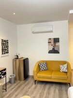 Una sala de estar moderna con un sofá amarillo, una mesa de centro, un televisor y un aire acondicionado instalado en la pared.