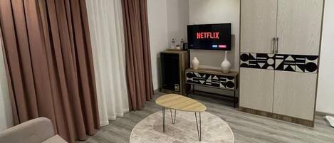 Ein modernes Wohnzimmer mit einer Couch, einem Couchtisch, einem Fernseher, der 'NETFLIX' anzeigt, und einem Schrank mit geometrischen Mustern.