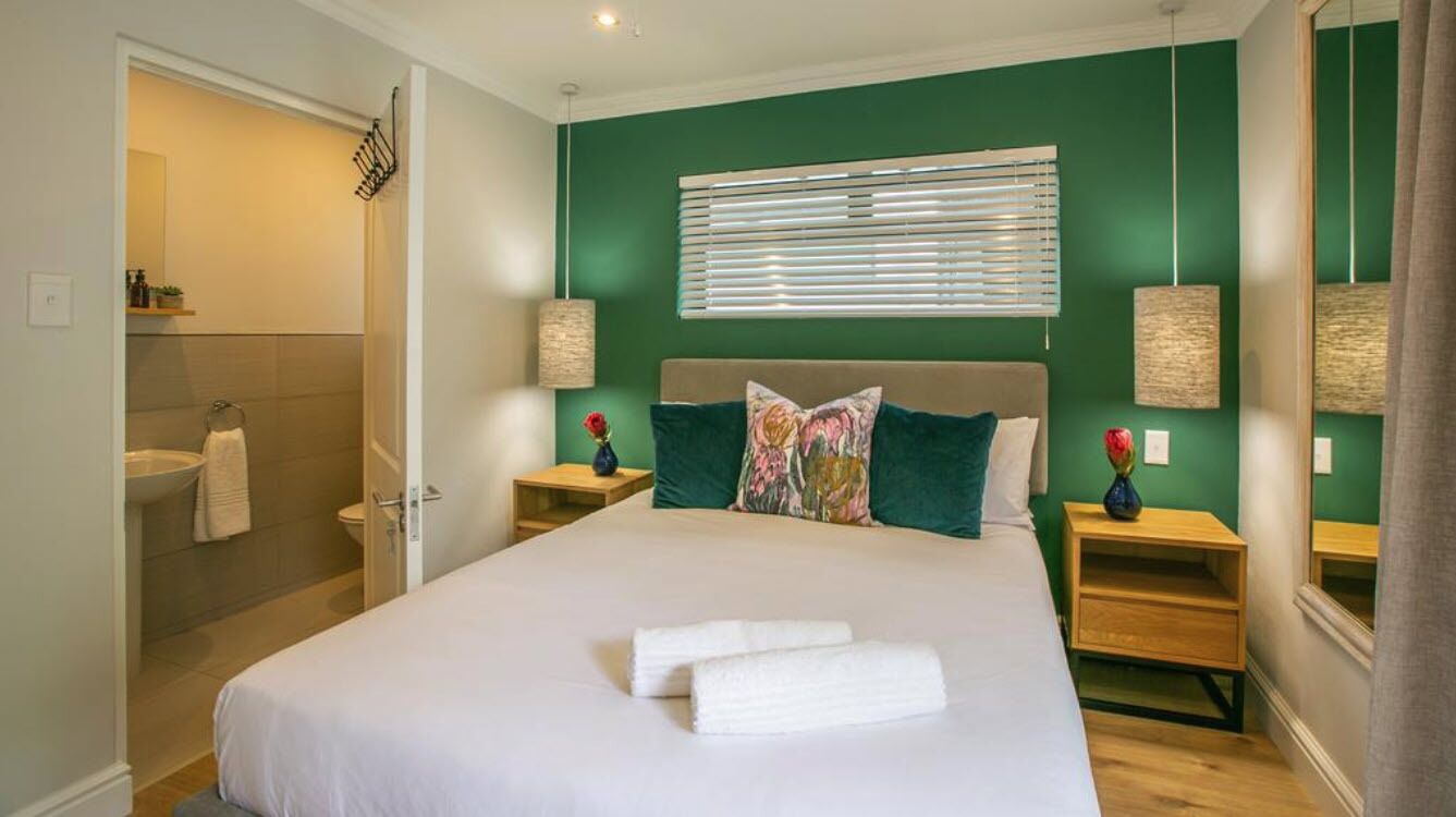 Een slaapkamer met een bed, twee nachtkastjes, een spiegel en een badkamer zichtbaar door een open deur.