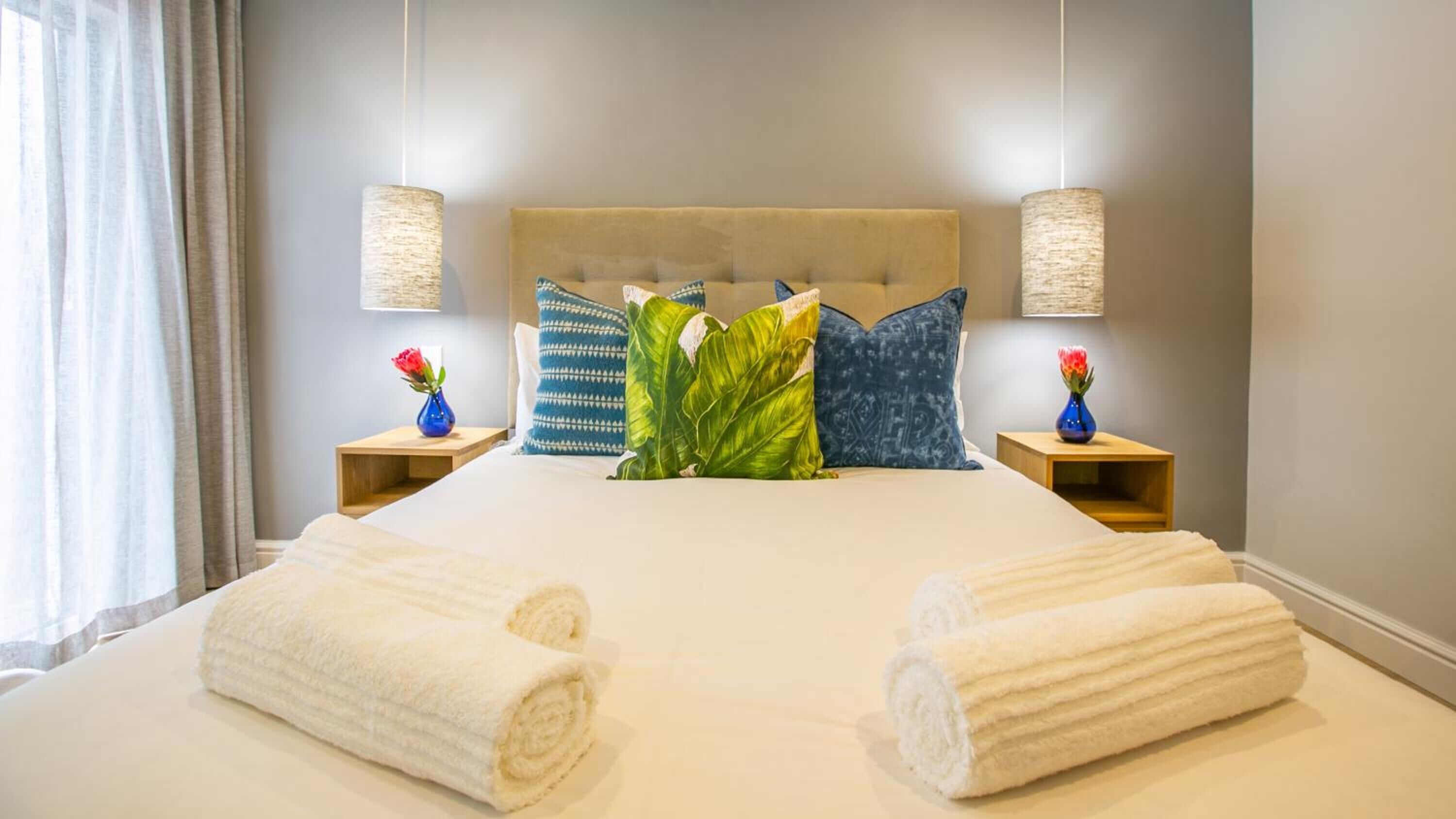 A neatly made bed with two rolled towels, a headboard, and decorative pillows.