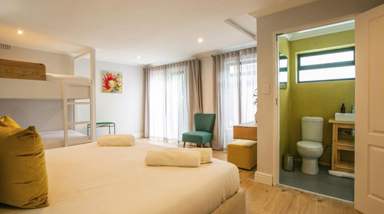 A hotel room with a bunk bed, a green armchair, a small table, and a bathroom with a toilet and sink.